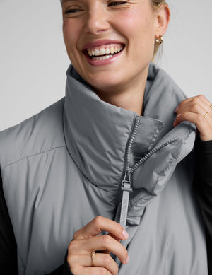 model wearing a gray puffer vest over a black long sleeve and leggings on a light gray background. 
