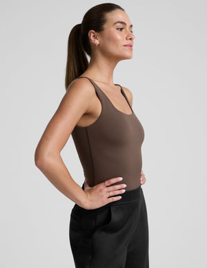 model wearing a brown square neck tank bodysuit and black pants against a plain background. 