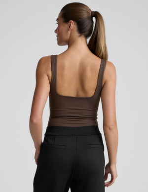 model wearing a brown square neck tank bodysuit and black pants against a plain background. 