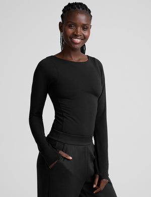 woman wearing a black long-sleeve boatneck bodysuit and black pants on a plain background. 