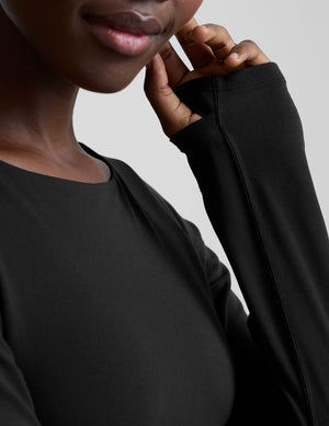 woman wearing a black long-sleeve boatneck bodysuit and black pants on a plain background. 