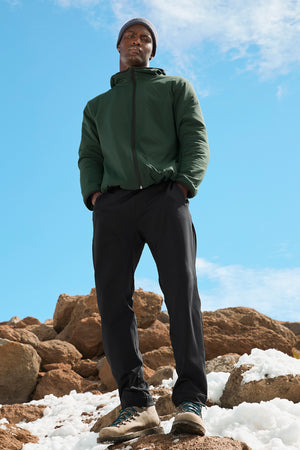Man wearing a green jacket and black pants standing in the snow. 