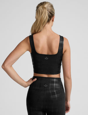 model wearing a black plaid foil printed square neck cropped tank top and matching leggings against a plain background. 