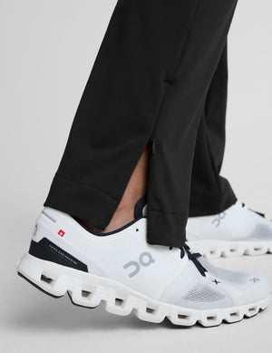 person wearing black pants and white sneakers on a light gray background