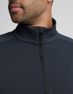 man wearing a dark blue quarter zip pullover against a plain background. 