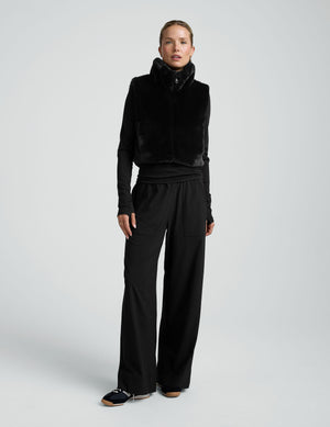 woman wearing a black faux fur vest against a plain background. 