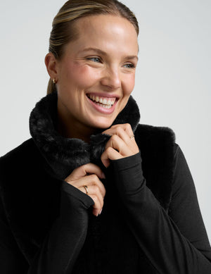 woman wearing a black faux fur vest against a plain background. 