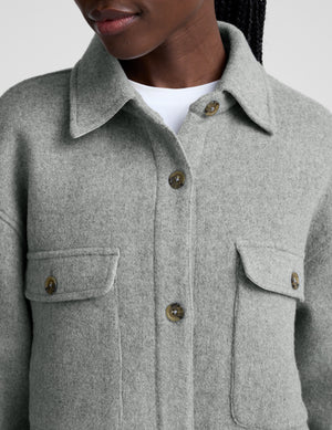 woman wearing a gray shirt jacket against a plain background. 