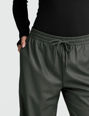 woman wearing a black long sleeve and green wide-leg faux leather pants against a plain background. 