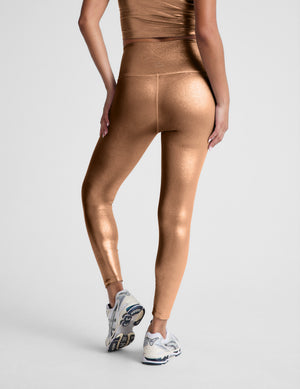woman wearing copper metallic midi leggings against a light gray background. 