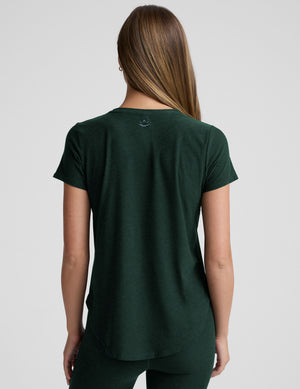 woman wearing a dark green t-shirt and leggings against a plain background. 