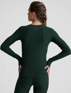 model wearing a green fitted crew neck long-sleeve top against a light gray background. 