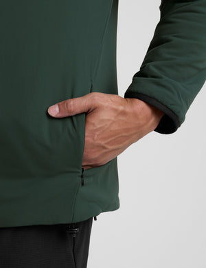 man wearing a green jacket with a hood on a gray background. 