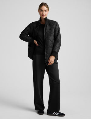 Woman wearing a black quilted and boucle jacket on a light gray background. 