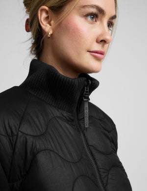 Woman wearing a black quilted and boucle jacket on a light gray background. 