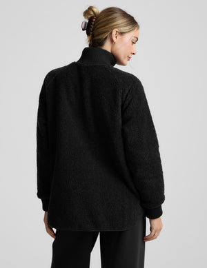 Woman wearing a black boucle jacket on a light gray background. 