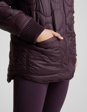 Woman wearing a quilted and boucle purple jacket on a light gray background. 