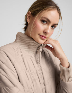Woman wearing a beige quilted and boucle jacket on a light gray background. 