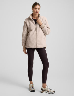 Woman wearing a beige quilted and boucle jacket on a light gray background. 