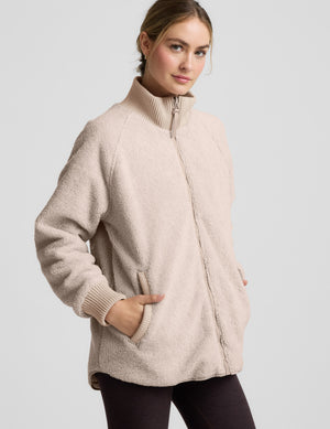 Woman wearing a beige quilted and boucle jacket on a light gray background. 