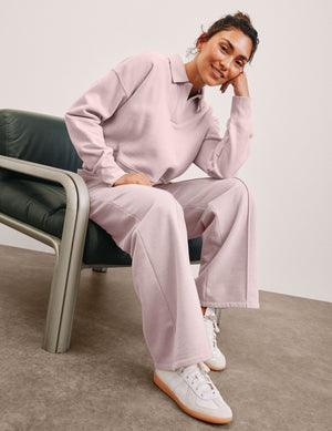 woman in a pink fleece sweatshirt and pink fleece pintuck pants sitting on a chair with a neutral background. 