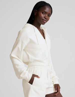 model wearing a white fleece zip-up hoodie and fleece sweat shorts with a drawcord at waistband on a plain background. 