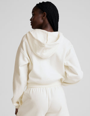 model wearing a white fleece zip-up hoodie and fleece sweat shorts with a drawcord at waistband on a plain background. 