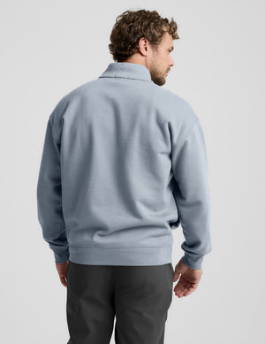 Man wearing a light blue half-zip sweatshirt against a plain background.