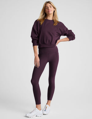 model wearing a purple fleece cropped crew neck sweatshirt and leggings on a light gray background. 
