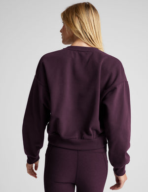 model wearing a purple fleece cropped crew neck sweatshirt and leggings on a light gray background. 