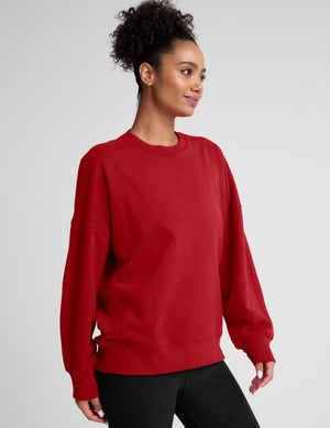 model wearing a red oversized crewneck fleece sweatshirt on a plain background. 