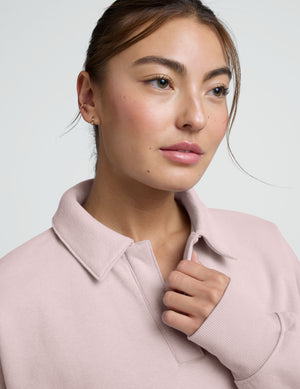 woman wearing a light pink collared sweatshirt and pants on a plain background. 