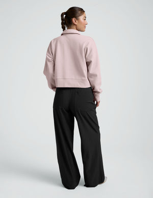 woman wearing a light pink collared sweatshirt and pants on a plain background. 