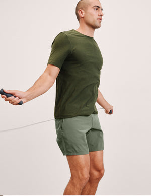 Man in green athletic wear using a jump rope on a light pink background. 