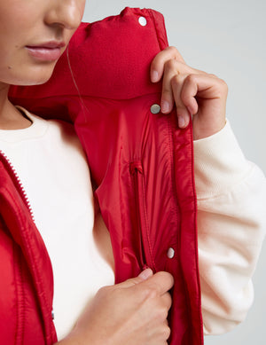 woman wearing a red puffer vest and leggings against a plain background. 