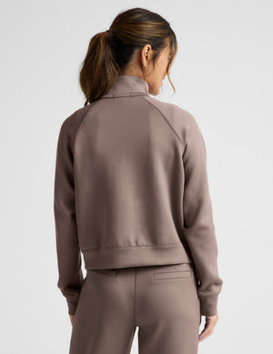 Woman wearing a brown tracksuit on a light gray background. 