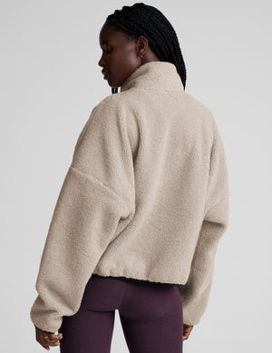 model wearing a beige zip-up fleece jacket against a plain background. 