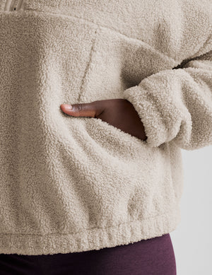 close-up of a person wearing a beige fleece jacket with a hand in the pocket.