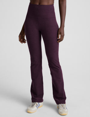 model wearing purple high-waisted bootcut pants with pockets on a plain background. 