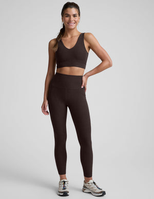 woman wearing a brown high-waisted midi length pocket leggings  with a plain background. 