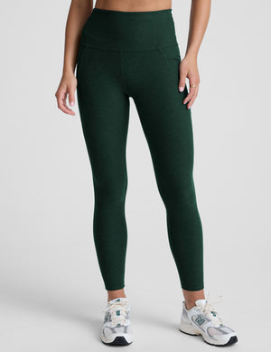 model is wearing green high-waisted midi length leggings with pockets on a plain background.