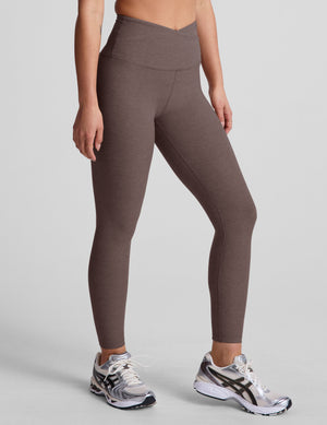Brown leggings with a crossover front waistband worn by a person on a plain background. 