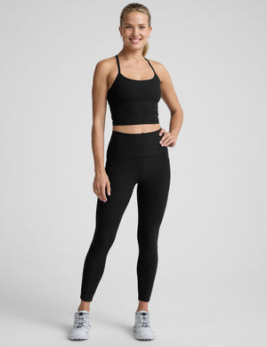 woman wearing a black racerback cropped tank and leggings on a plain background. 