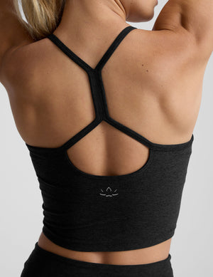 woman wearing a black racerback cropped tank and leggings on a plain background. 