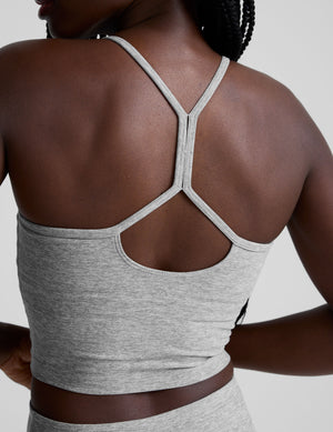 woman is wearing a gray racerback cropped tank and gray leggings against a plain background. 