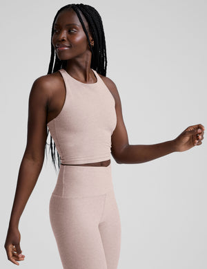 model wearing a beige high neck racerback cropped tank top and beige high-waisted midi length leggings against a plain background. 