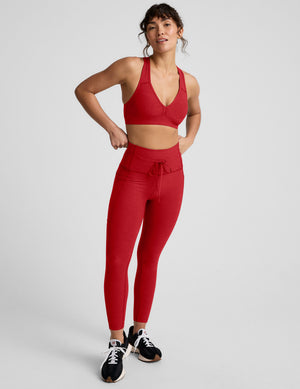 Woman wearing a red v-neck bra and leggings on a light background. 