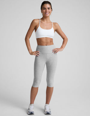 woman wearing a white slim racerback sports bra and gray leggings on a plain background. 