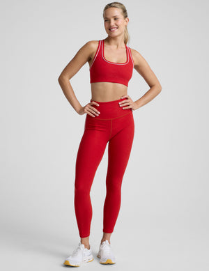 Woman wearing a red sports bra and leggings with white piping on a light background. 