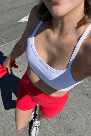 model is wearing a white bra and red high-waisted biker shorts. 
